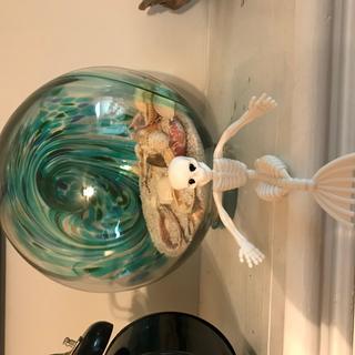 Mermaid skelly sits on the mantle in front of a glass ball beach scene